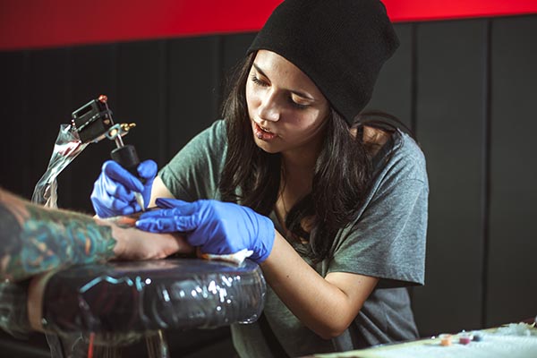 Attractive young female tattoo artist tattooing a customer