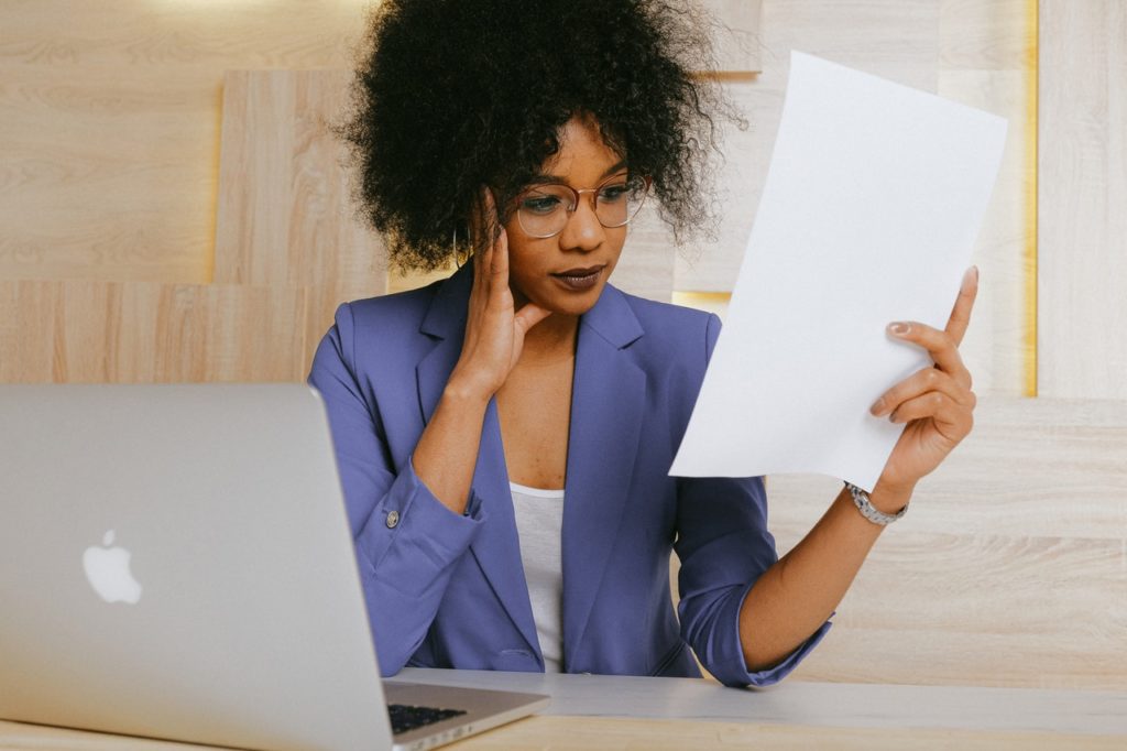 Woman looking at piece of paper with laptop