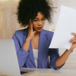 Woman looking at piece of paper with laptop